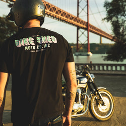 Model wearing a 'Bike Shed Moto Co.' graphic logo t-shirt with a motorcycle and bridge in the background.