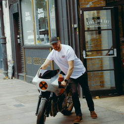 Model wearing Bike Shed Motorcycle Race T-Shirt White next to a custom motorcycle.