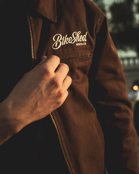 Model wearing the Bike Shed Moto Co Twill brown jacket with a Bike Shed brand logo.