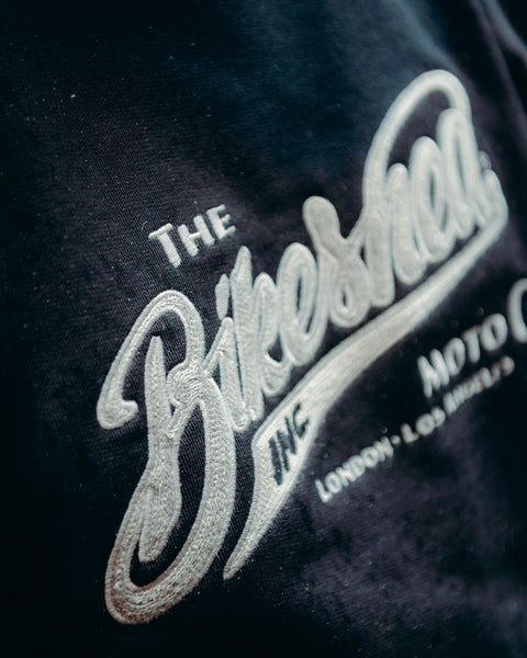 Model wearing Bike Shed Moto Co Black Applique Sweatshirt next to a motorcycle on a brick driveway