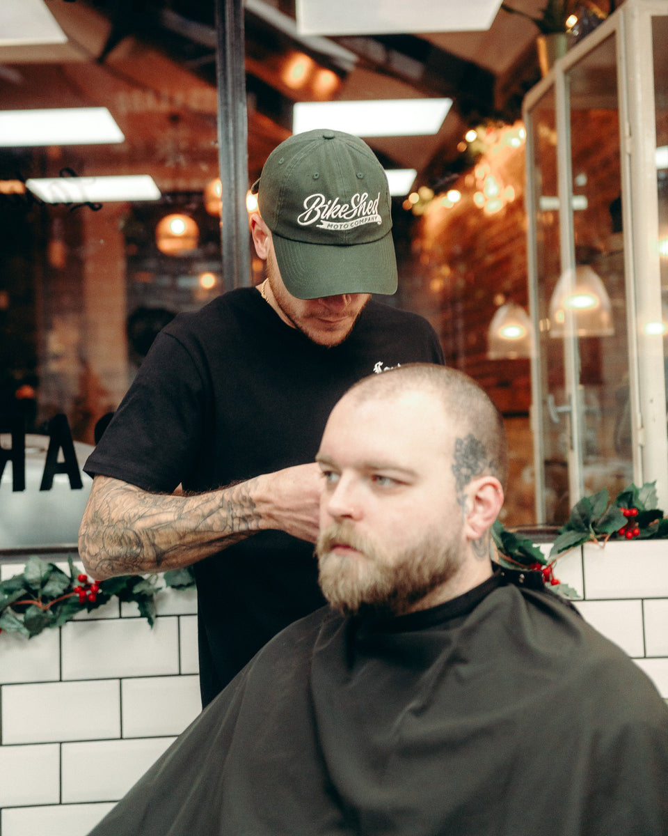 Model wearing Bike Shed Moto Script cap in green while cutting hair