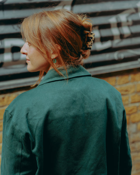 Model wearing green motorcycle jacket in front of a brick wall with graffiti.