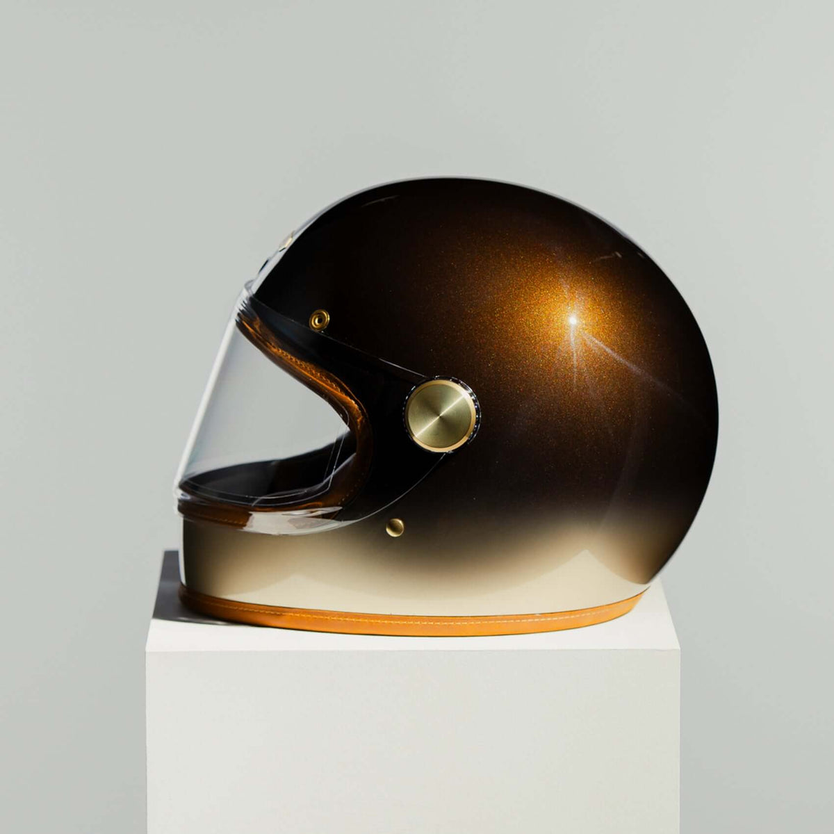 Gold and black helmet on a white pedestal with a gray background