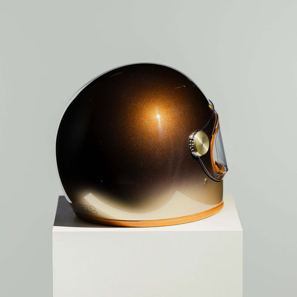Bronze-colored helmet on a white pedestal against a gray background