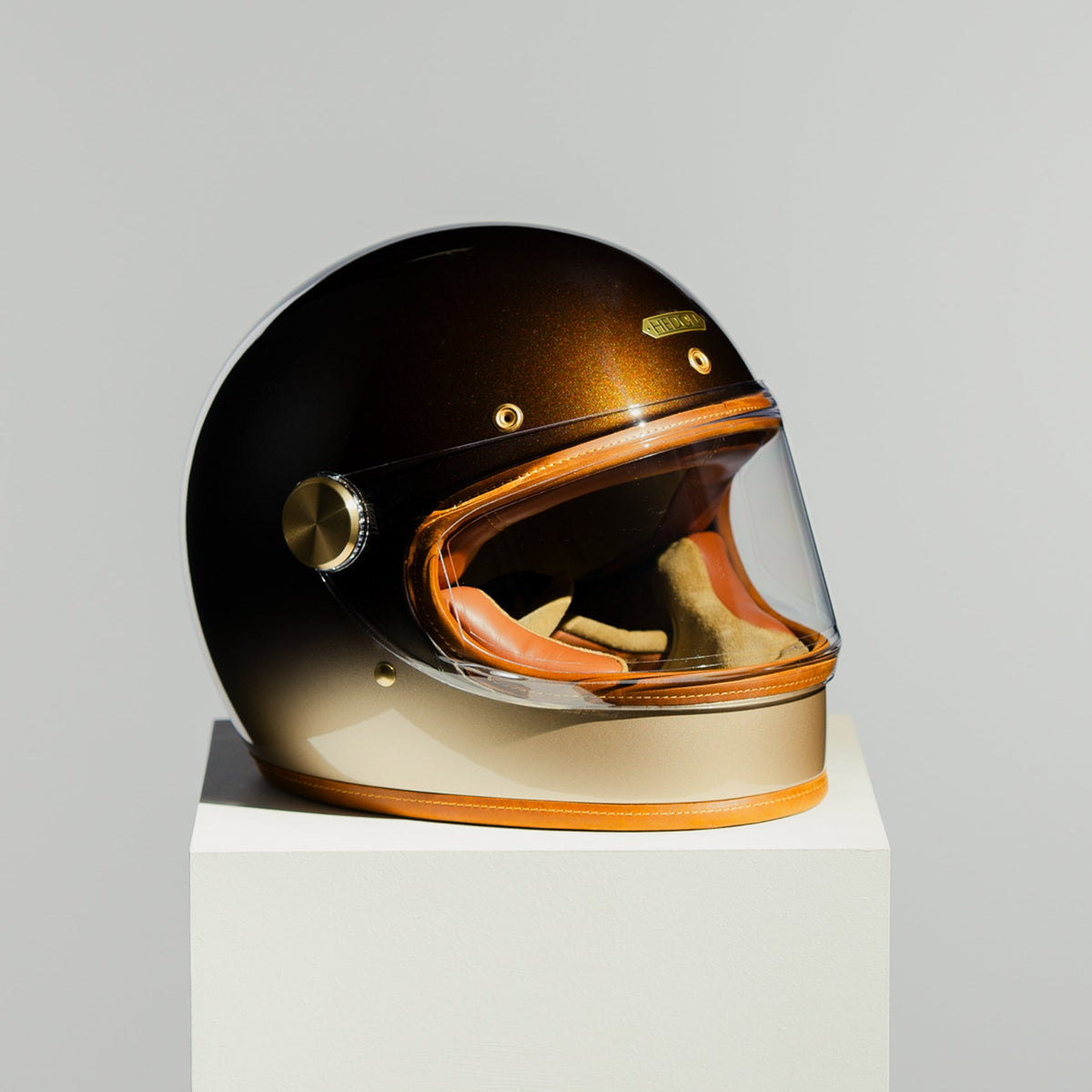 Helmet with gold and black finish on a white pedestal against a gray background